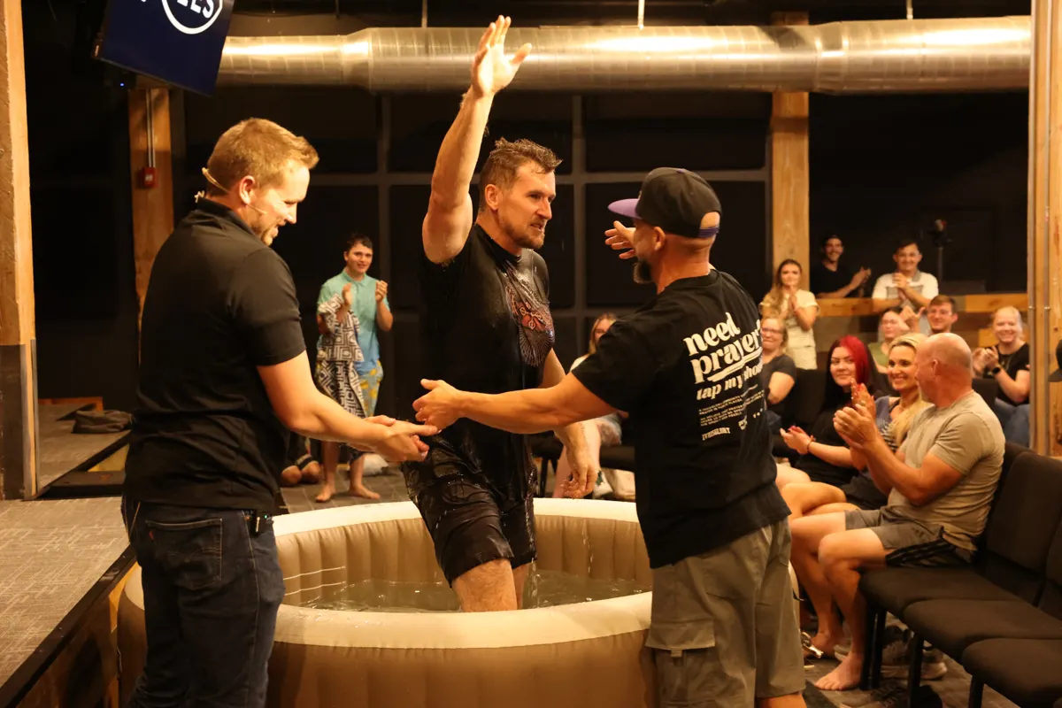 A newly baptized man raises his fist in celebration as two church leaders cheer beside the baptism pool